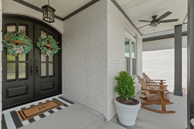 view of exterior entry featuring brick siding, a porch, a ceiling fan, and french doors