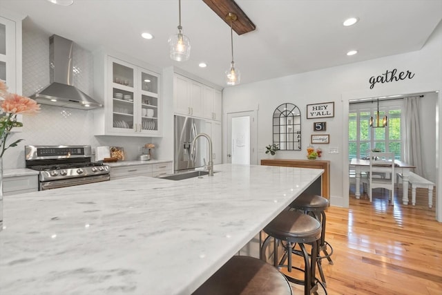 kitchen featuring light wood finished floors, wall chimney exhaust hood, gas stove, a sink, and a kitchen breakfast bar