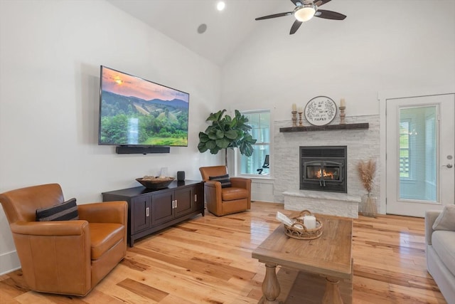 living area featuring light wood-style flooring, a fireplace, high vaulted ceiling, and a ceiling fan