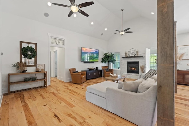 living room with light wood finished floors, a warm lit fireplace, high vaulted ceiling, and ceiling fan