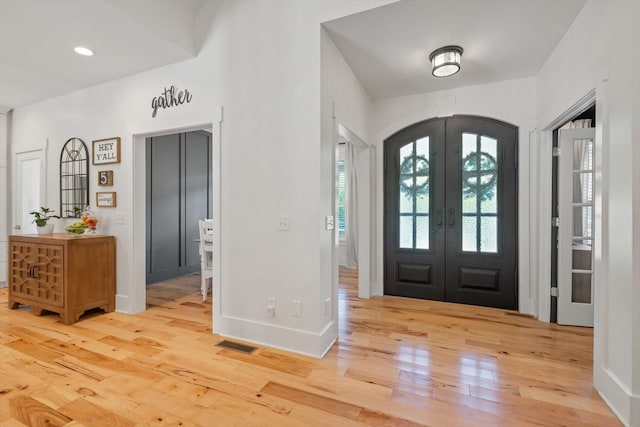 entrance foyer featuring arched walkways, french doors, visible vents, baseboards, and hardwood / wood-style flooring