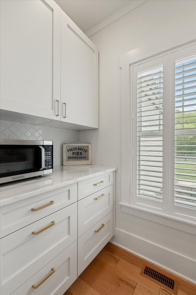 room details featuring light wood finished floors, visible vents, stainless steel microwave, backsplash, and white cabinetry