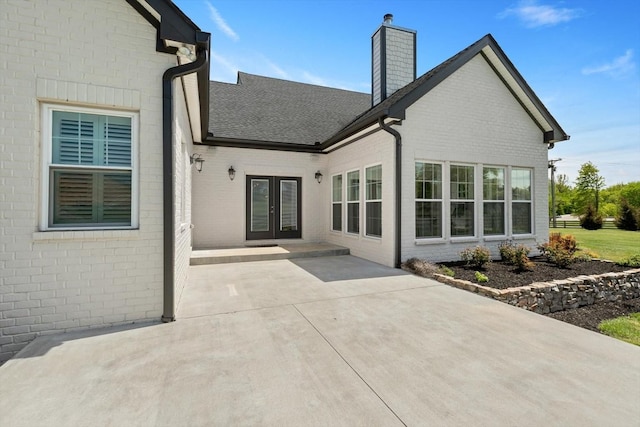 rear view of property featuring french doors, brick siding, roof with shingles, a chimney, and a patio area