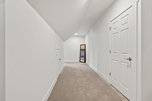 hallway with baseboards, lofted ceiling, and light colored carpet