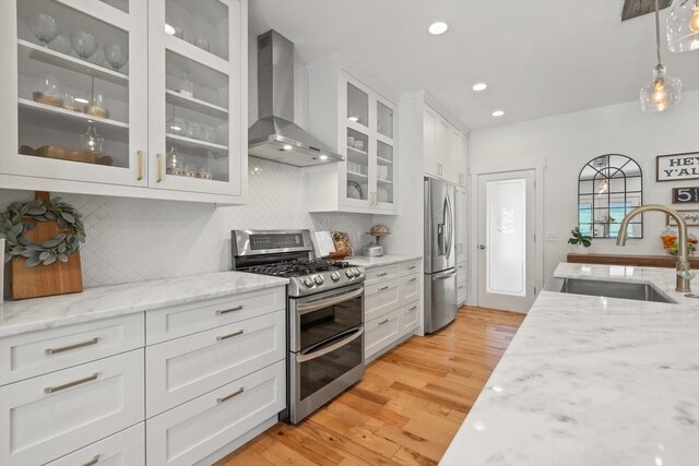 kitchen with decorative backsplash, white cabinets, wall chimney exhaust hood, appliances with stainless steel finishes, and a sink