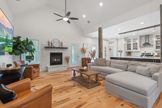 living area with ceiling fan, high vaulted ceiling, a fireplace, light wood-style floors, and ornate columns