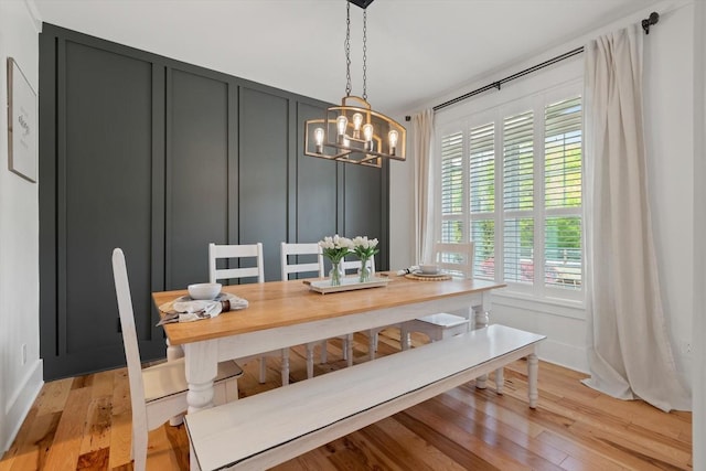 dining space with light wood-style flooring, a decorative wall, and a notable chandelier