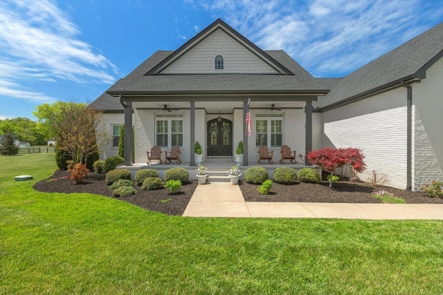 view of front of house featuring a shingled roof, ceiling fan, covered porch, french doors, and a front lawn