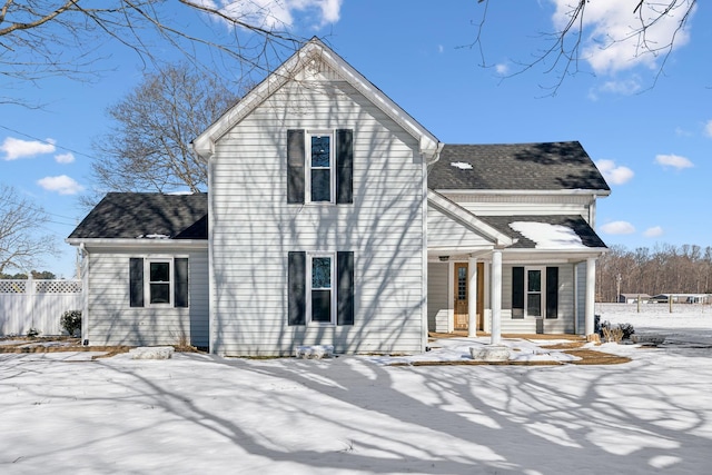 snow covered property with a shingled roof and fence