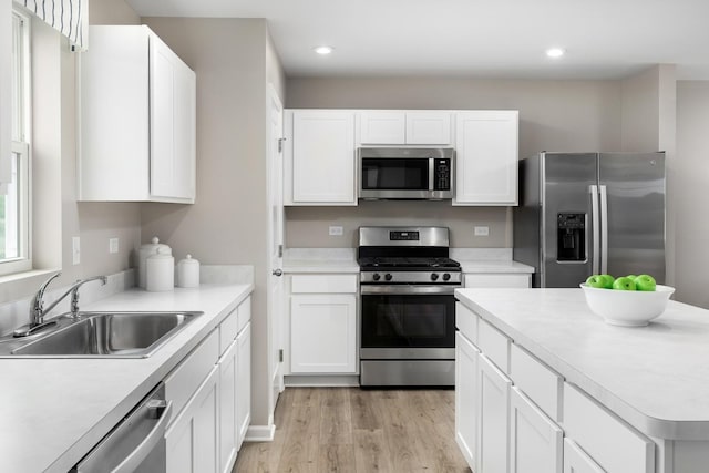 kitchen featuring light wood finished floors, light countertops, stainless steel appliances, white cabinetry, and a sink