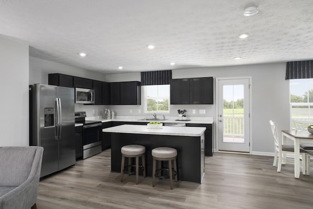 kitchen featuring a center island, dark cabinets, a breakfast bar, appliances with stainless steel finishes, and a sink