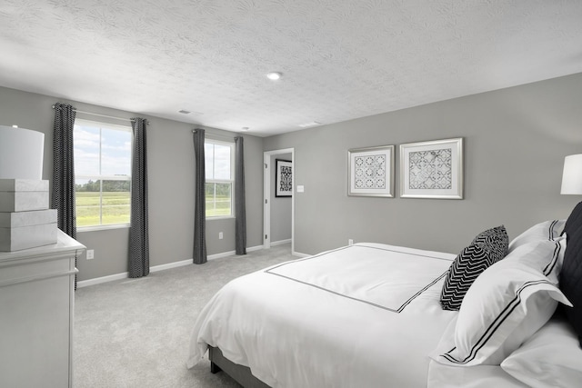 bedroom with baseboards, light colored carpet, and a textured ceiling