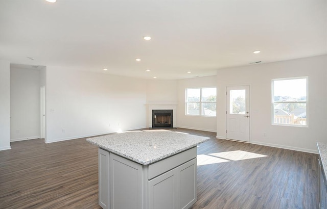 unfurnished living room with dark wood-style flooring, plenty of natural light, a fireplace with flush hearth, and recessed lighting