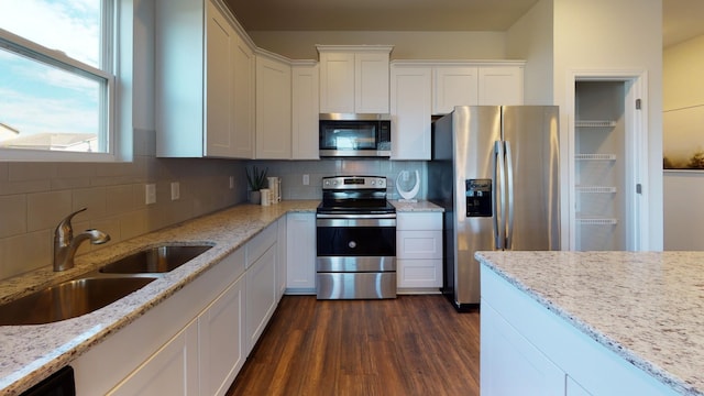 kitchen with stainless steel appliances, a sink, white cabinets, backsplash, and dark wood-style floors