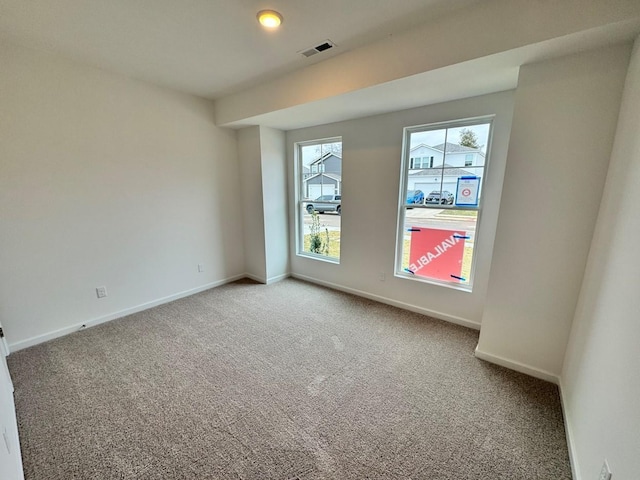 empty room featuring light colored carpet, visible vents, and baseboards