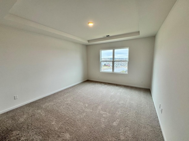 carpeted spare room with visible vents, a tray ceiling, and baseboards