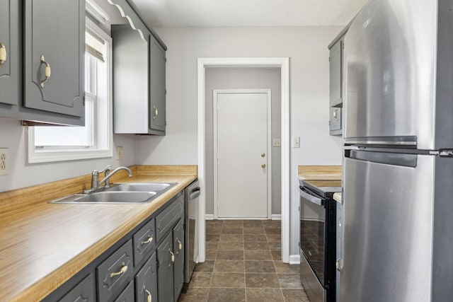 kitchen featuring gray cabinetry, a sink, baseboards, light countertops, and appliances with stainless steel finishes