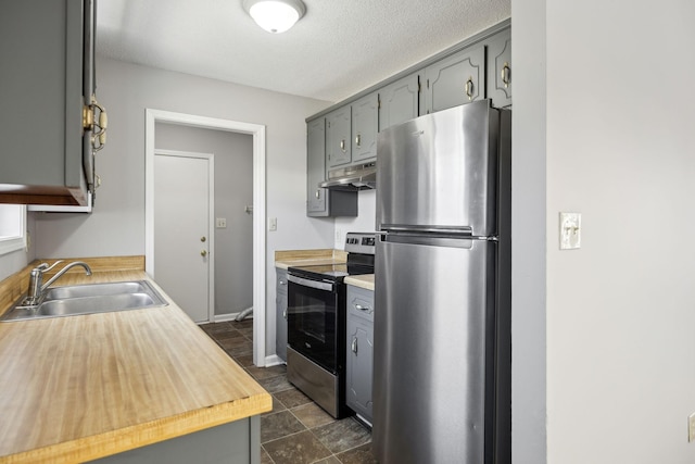 kitchen featuring gray cabinetry, appliances with stainless steel finishes, a sink, a textured ceiling, and under cabinet range hood