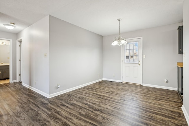 unfurnished dining area featuring a notable chandelier, a textured ceiling, baseboards, and dark wood-type flooring