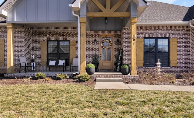 property entrance with roof with shingles, a lawn, board and batten siding, and brick siding