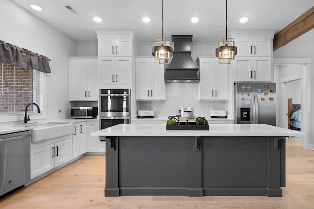 kitchen featuring stainless steel appliances, a sink, white cabinetry, light countertops, and custom range hood