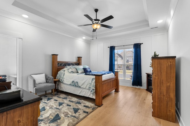 bedroom with light wood finished floors, visible vents, a raised ceiling, and a ceiling fan