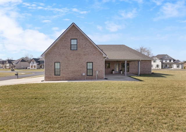 back of house featuring brick siding, a yard, a patio, a shingled roof, and a residential view