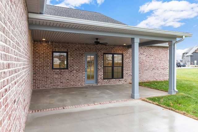 entrance to property with brick siding, a patio, a lawn, a ceiling fan, and driveway