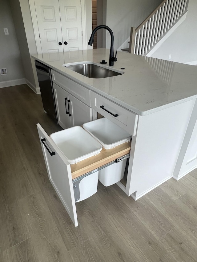 kitchen featuring wood finished floors, a sink, white cabinets, black dishwasher, and an island with sink