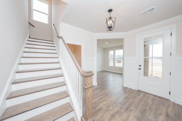 foyer entrance featuring visible vents, wainscoting, ornamental molding, wood finished floors, and a decorative wall