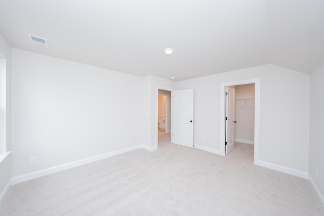 unfurnished bedroom featuring light carpet, a spacious closet, visible vents, and baseboards