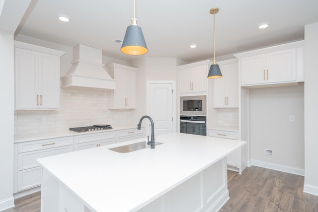 kitchen with premium range hood, a sink, white cabinets, appliances with stainless steel finishes, and a center island with sink