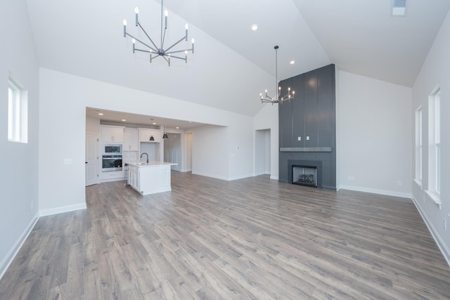 unfurnished living room with high vaulted ceiling, a fireplace, light wood-style flooring, and an inviting chandelier