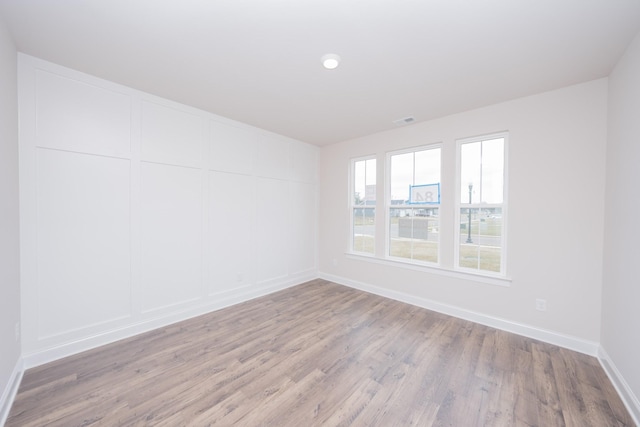 unfurnished room featuring light wood finished floors, a decorative wall, and baseboards