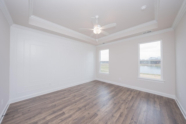 spare room with dark wood-type flooring, visible vents, baseboards, a raised ceiling, and crown molding