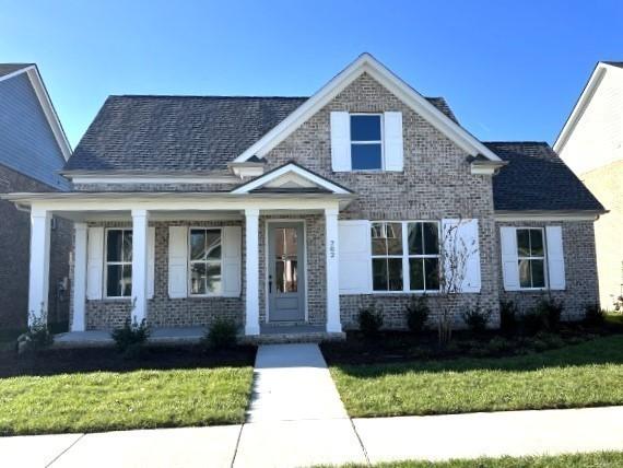 view of front of house featuring covered porch, brick siding, and a front yard