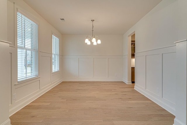 unfurnished dining area featuring a chandelier, visible vents, light wood-style flooring, and a decorative wall