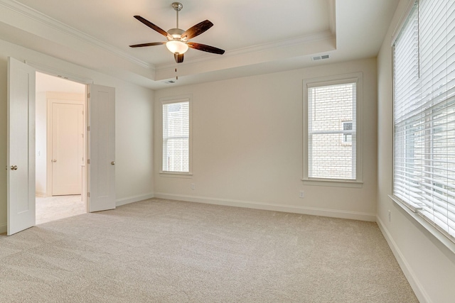 spare room with light carpet, visible vents, baseboards, ornamental molding, and a tray ceiling