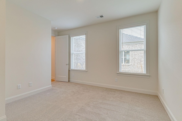 unfurnished room featuring a healthy amount of sunlight, visible vents, light carpet, and baseboards