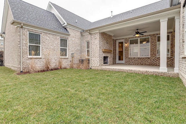 rear view of property with ceiling fan, a shingled roof, brick siding, a yard, and a patio area