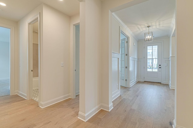 entrance foyer featuring light wood-type flooring, a wainscoted wall, crown molding, and a decorative wall