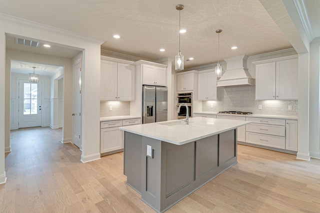 kitchen with visible vents, appliances with stainless steel finishes, a sink, light wood-type flooring, and premium range hood