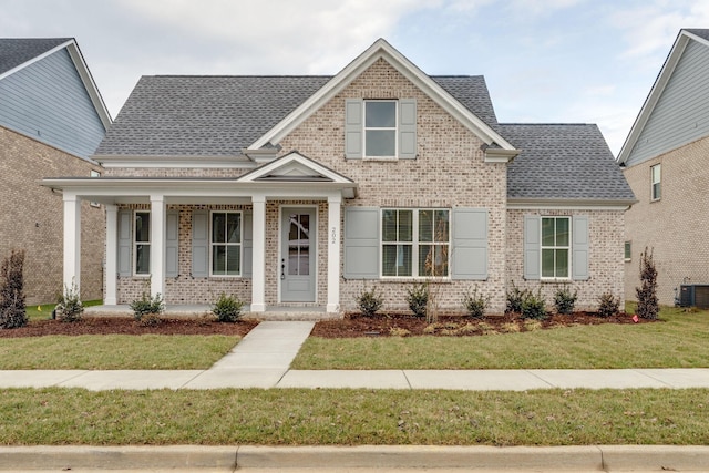 view of front facade with brick siding, a porch, a front yard, and a shingled roof