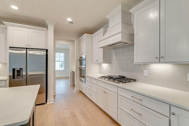 kitchen with custom exhaust hood, light wood finished floors, appliances with stainless steel finishes, and light countertops