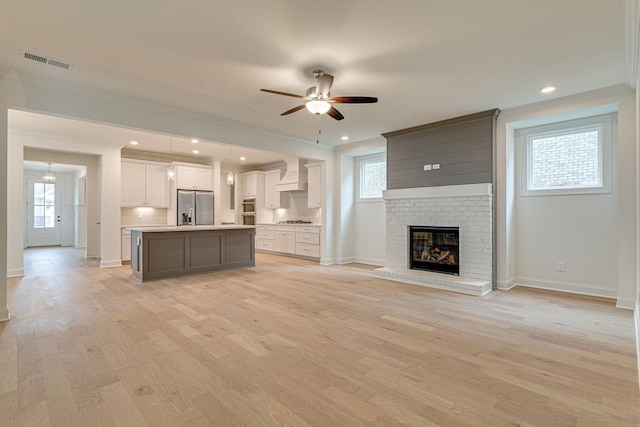 unfurnished living room with a healthy amount of sunlight, light wood finished floors, visible vents, and crown molding