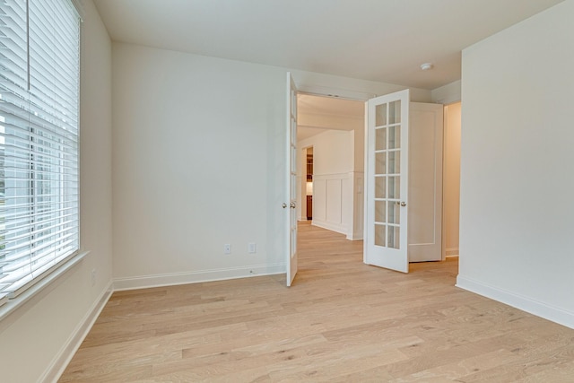 spare room featuring french doors, baseboards, and light wood finished floors