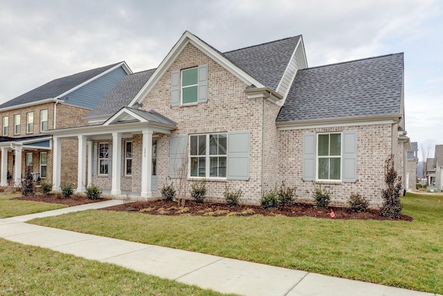 craftsman inspired home featuring a shingled roof, a front yard, brick siding, and a porch