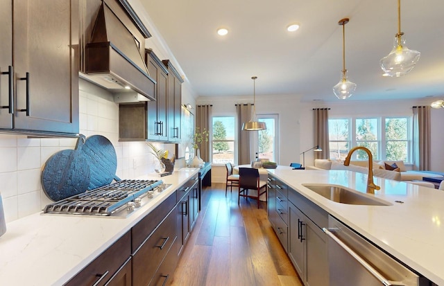 kitchen featuring hanging light fixtures, appliances with stainless steel finishes, a sink, wood finished floors, and premium range hood