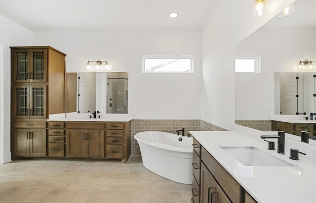 full bath featuring a stall shower, a soaking tub, two vanities, and a sink