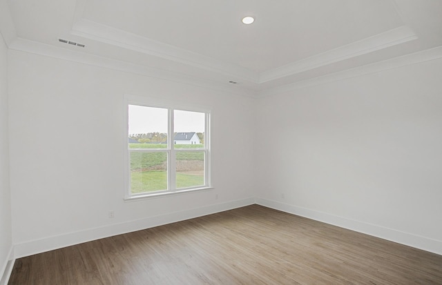 spare room featuring wood finished floors, a raised ceiling, visible vents, and crown molding